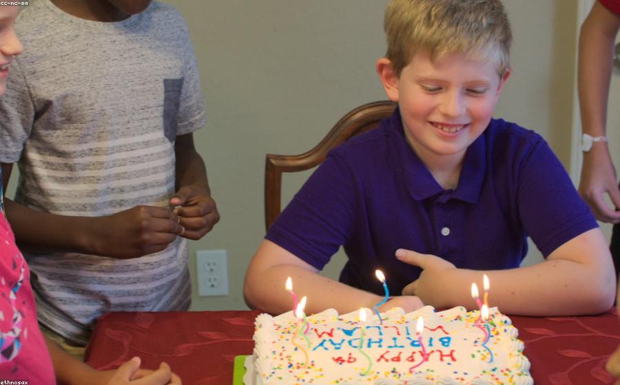 A child smiling at a birthday cake with lit candles at a party