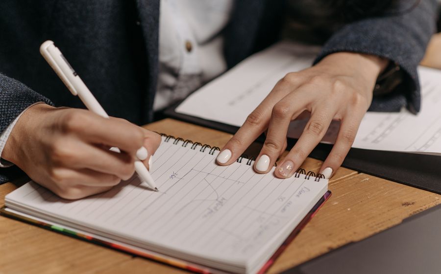 A person writing by hand in a spiral notebook