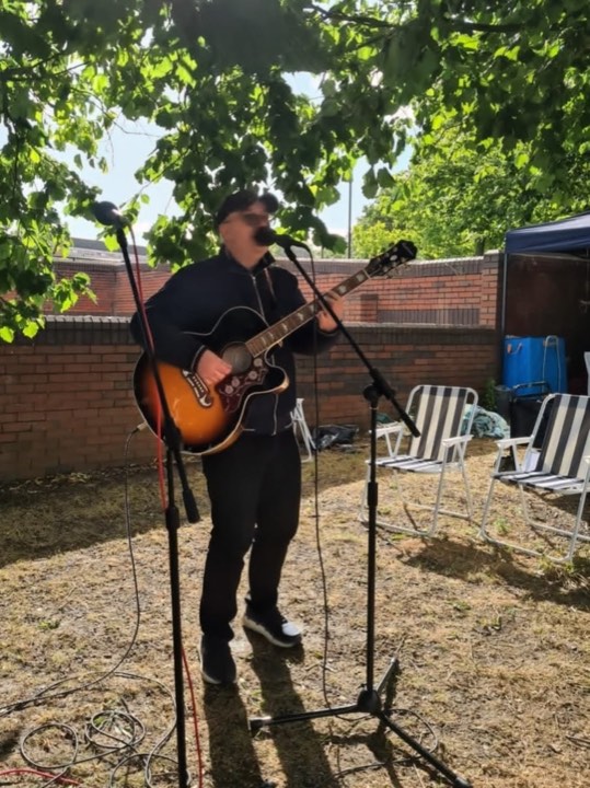 Edwin outdoors with a guitar beside a brick wall